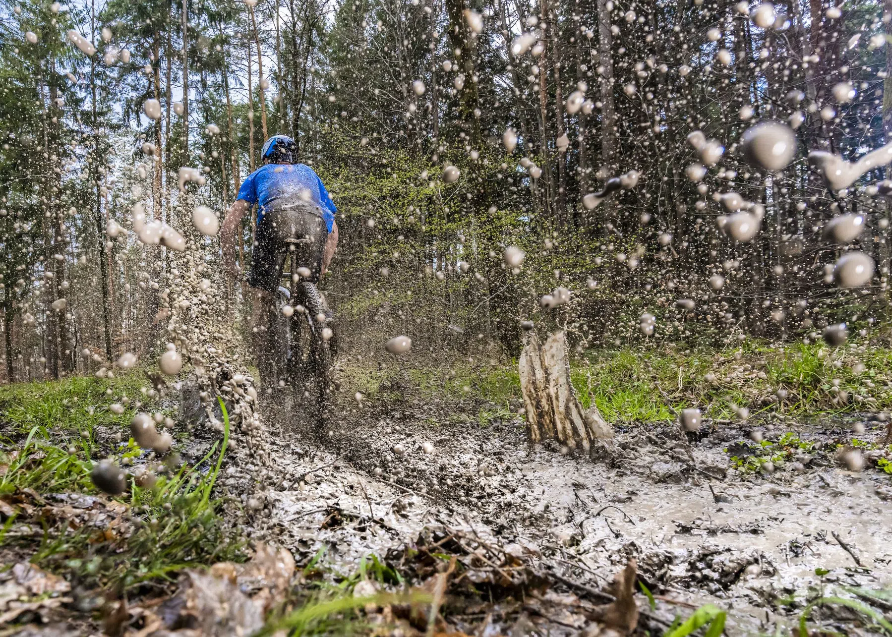Een mountainbiker spetters door een grote plas modder in het bos
